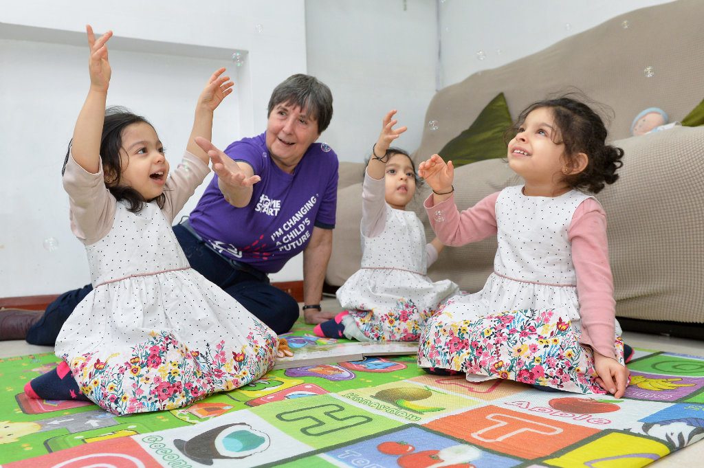 Volunteer volunteer playing with triplet girls on floor